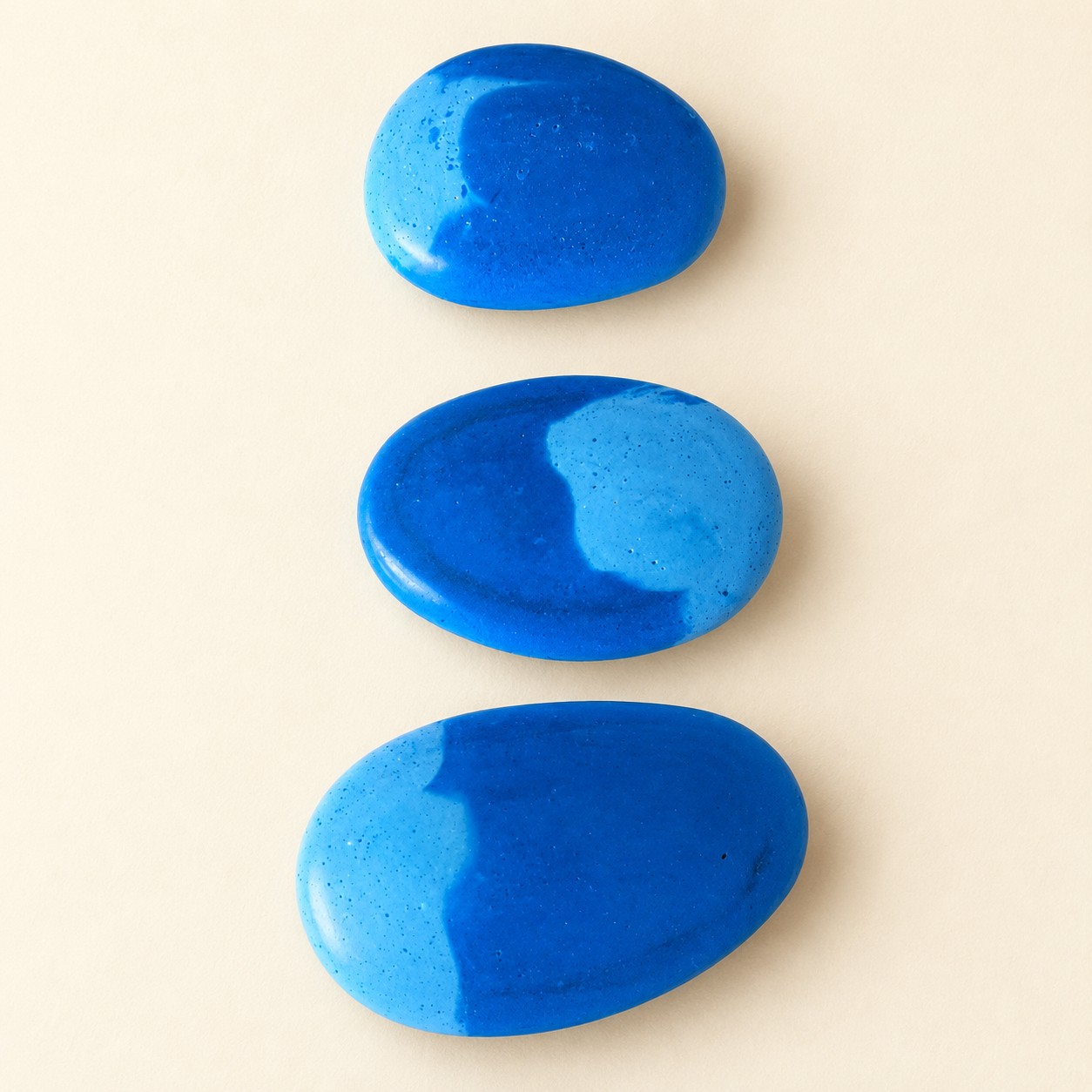 Illustrative mockup of three blue scented pebbles on a cream background